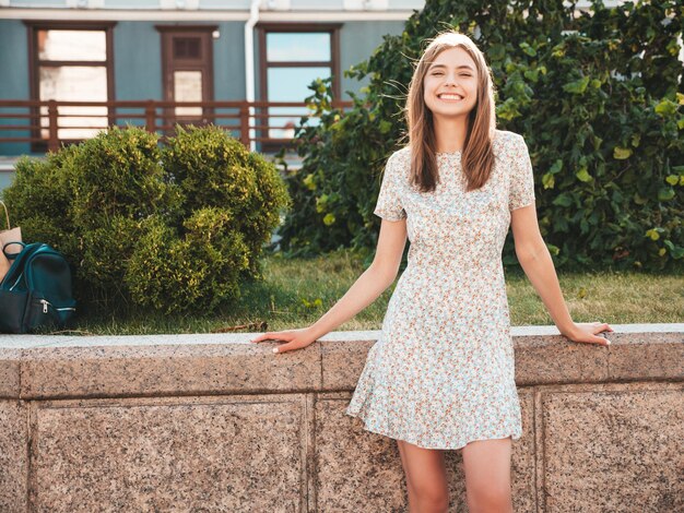 Jonge mooie lachende hipster vrouw in trendy zomerjurk Sexy zorgeloze vrouw poseren op de straat achtergrond bij zonsondergang Positief model buitenshuis vrolijk en blij met handtas