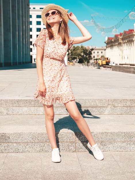 Jonge mooie lachende hipster vrouw in trendy zomerkleren Sexy zorgeloze vrouw die zich voordeed op de straat achtergrond bij zonsondergang Positief model buitenshuis vrolijk en gelukkig in zonnebril en hoed