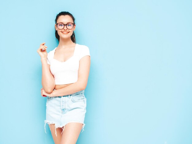 Jonge mooie lachende vrouw in trendy zomer jeans rok en top kleding Sexy zorgeloze vrouw poseren in de buurt van blauwe muur in studio Positieve brunette model plezier vrolijk en gelukkig