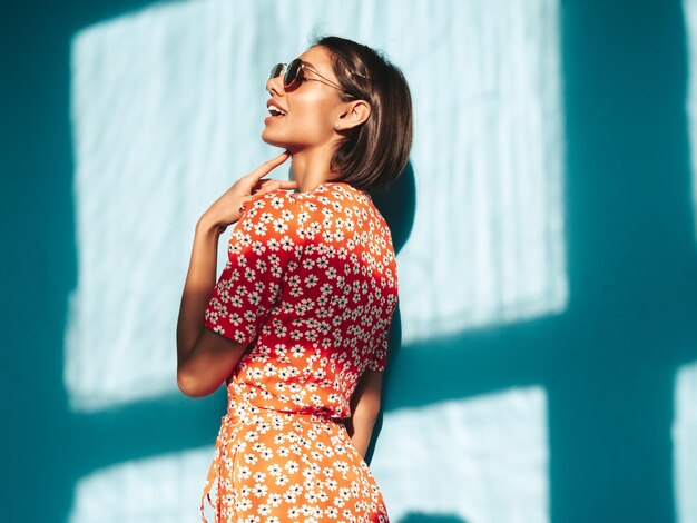 Jonge mooie lachende vrouw in trendy zomer rode jurk Sexy zorgeloze vrouw poseren in de buurt van blauwe muur in studio Positief model plezier vrolijk en gelukkig op zonnige dag schaduw van raam