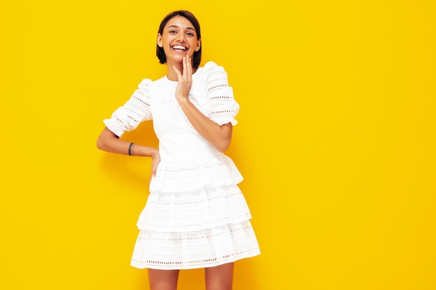 Jonge mooie lachende vrouw in trendy zomer witte jurk Sexy zorgeloze vrouw poseren in de buurt van gele muur in studio Positief model plezier vrolijk en gelukkig geïsoleerd