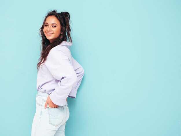 Jonge mooie lachende vrouw in trendy zomerkleren Sexy zorgeloze vrouw poseren in de buurt van blauwe muur in studio Positieve brunette model plezier en gek vrolijk en gelukkig