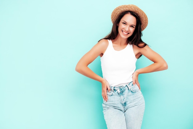 Jonge mooie lachende vrouw in trendy zomerkleren zorgeloze vrouw poseren in de buurt van blauwe muur in studio positieve brunette model plezier vrolijk en gelukkig in hat