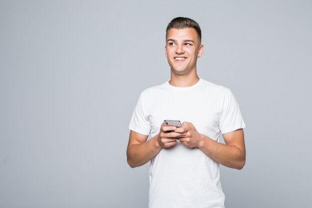 Jonge mooie man in een wit T-shirt geïsoleerd op wit houdt telefoon in zijn handen