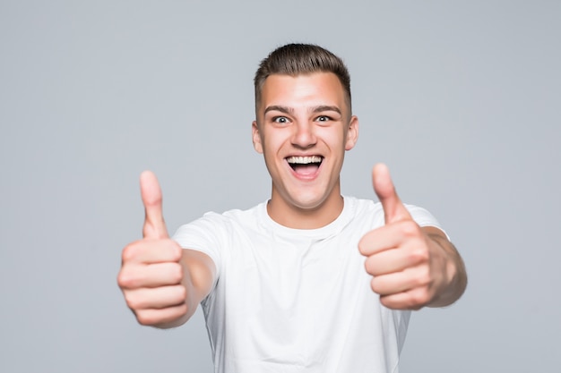 Jonge mooie man in een wit T-shirt op wit wordt geïsoleerd houden duimen omhoog