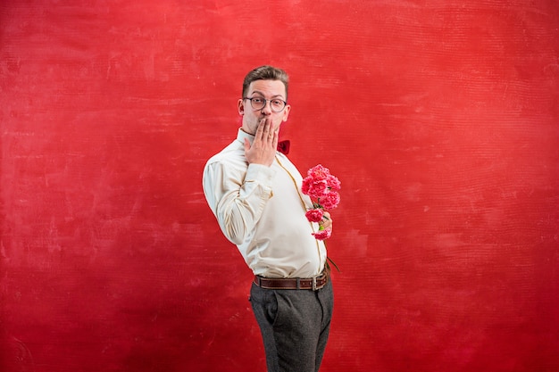 Gratis foto jonge mooie man met bloemen op rode studio achtergrond