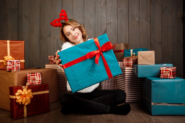 Jonge mooie meisjeszitting onder Kerstmisgiften over houten muur