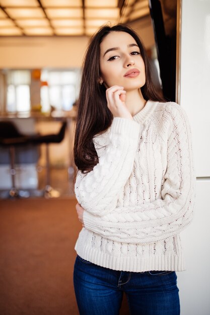 Jonge mooie model met grote ogen rode lippen en lang bruin haar in spijkerbroek blijven in de kamer bij haar thuis