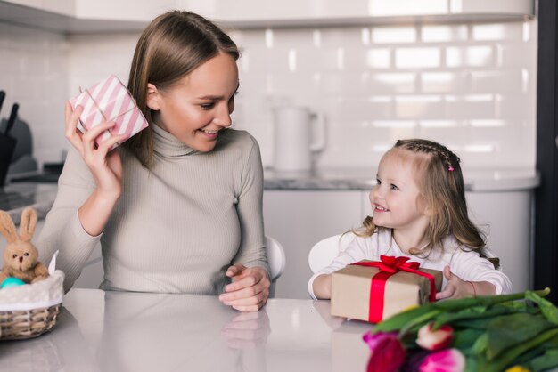 Jonge mooie moeder en dochter met geschenken doos in de keuken