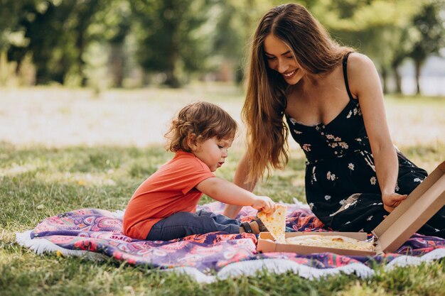 Jonge mooie moeder met kleine babyjongen eet pizza in park