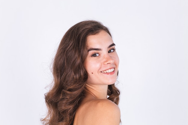 Jonge mooie natuurlijke zachte schone huid vrouw met sproeten lichte make-up op witte muur met blote schouders
