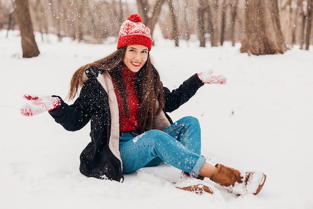 Jonge mooie openhartige lachende gelukkige vrouw in rode wanten en gebreide muts dragen zwarte jas wandelen spelen in park in de sneeuw, warme kleren, plezier