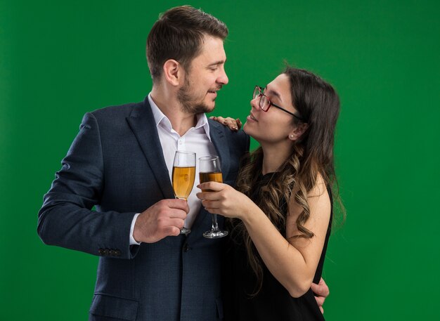Jonge mooie paar gelukkige man en lachende vrouw met glazen champagne omarmen kijken elkaar gelukkig verliefd samen vieren Valentijnsdag staande over groene muur