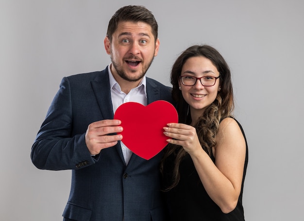 Jonge mooie paar gelukkige man en vrouw met rood hart glimlachend vrolijk gelukkig in liefde samen vieren van valentijnsdag