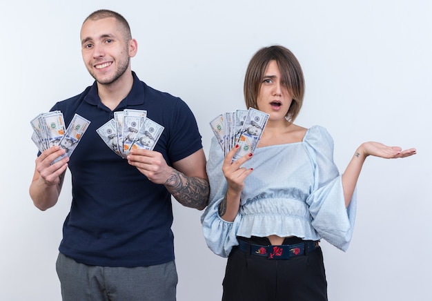 Jonge mooie paar in vrijetijdskleding man en vrouw met contant geld kijken glimlachend vrolijk staand