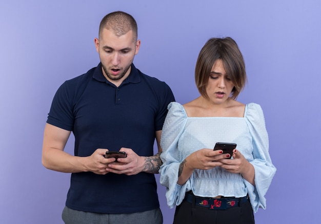 Jonge mooie paar man en vrouw met smartphones die verbaasd en verbaasd staan kijken