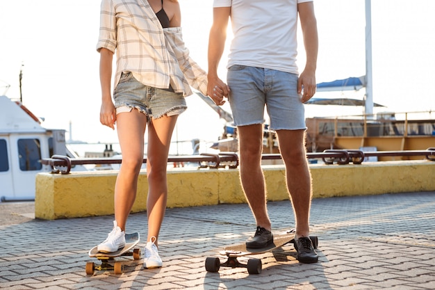 Jonge mooie paar wandelen aan zee, skateboarden. Close up van benen.