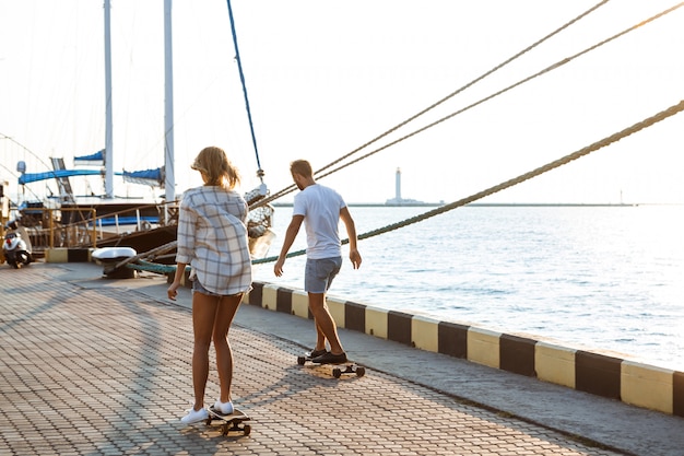 Jonge mooie paar wandelen aan zee, skateboarden.