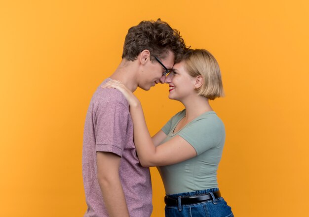 Jonge mooie paarman en vrouw die vrijetijdskleding dragen die zich gelukkig in liefde verenigen die over oranje muur koesteren