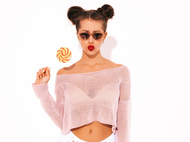 Jonge mooie sexy hipster vrouw met rode lippen in zonnebril. Trendy meisje in zomer badmode kleding. Snoeplolly eten