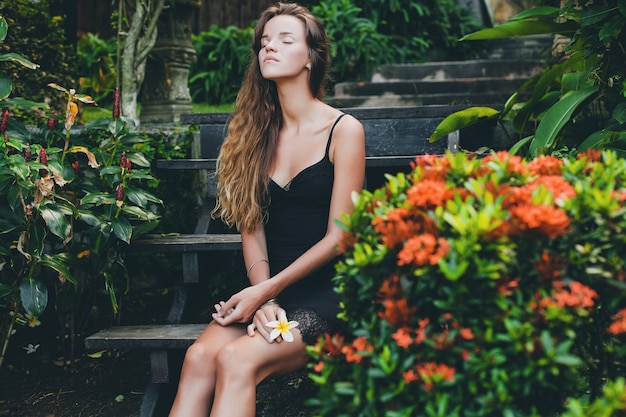 Jonge mooie sexy vrouw in tropische tuin, zomervakantie in thailand, slank mager gebruind lichaam, kleine zwarte jurk met kant, natuurlijke look, sensueel, ontspannen,