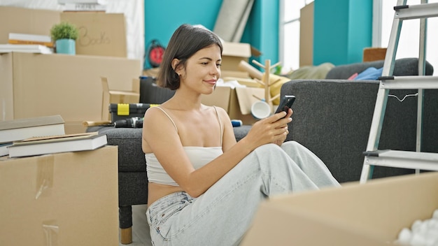 Gratis foto jonge mooie spaanse vrouw met behulp van smartphone zittend op de vloer in een nieuw huis