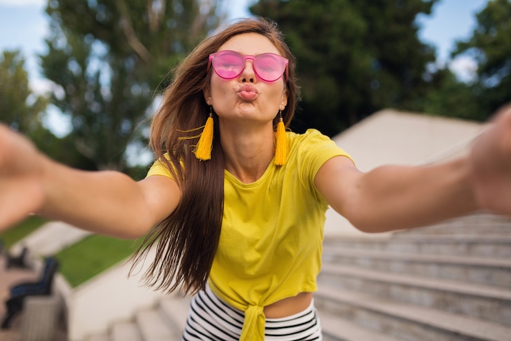 Gratis Foto jonge mooie stijlvolle lachende vrouw selfie maken in stadspark, positief, emotioneel, gele top, roze zonnebril, zomer stijl modetrend, lang haar, plezier dragen