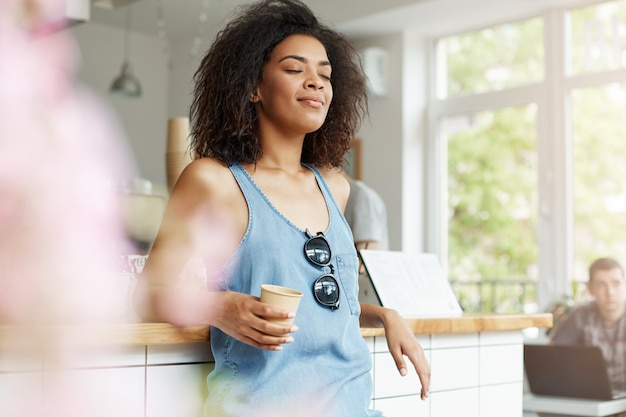 Jonge mooie tevreden Afrikaanse vrouw die het drinken koffie het rusten het ontspannen in koffie glimlachen. Gesloten ogen.