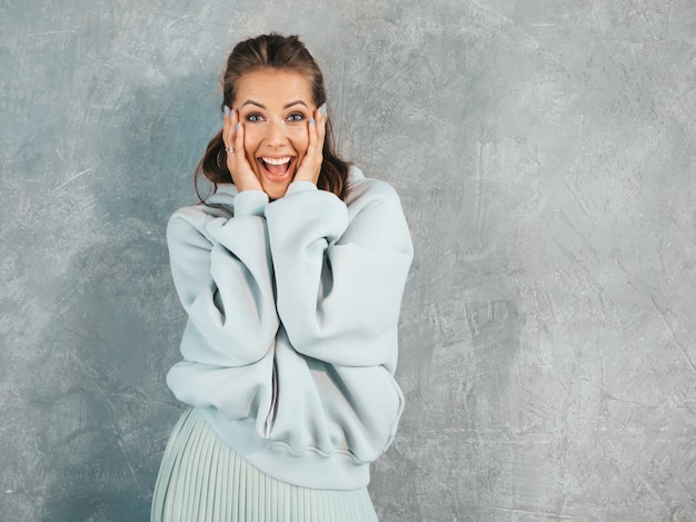 Jonge mooie verraste vrouw die met handen dichtbij gezicht kijkt. Trendy meisje in casual zomerkleding.