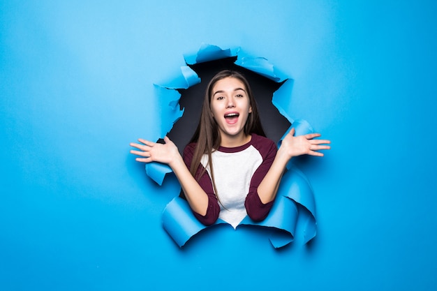 Jonge mooie verraste vrouw het kijken door blauw gat in document muur.