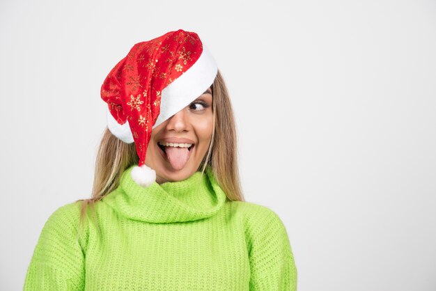 Jonge mooie vrouw die een grappig gezicht doet en in de rode hoed van de Kerstman stelt