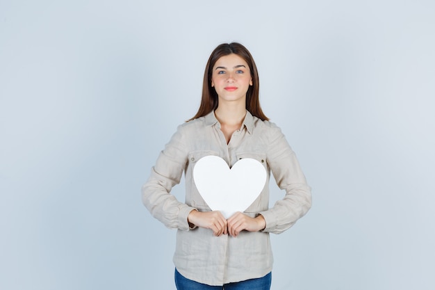 Jonge mooie vrouw die een papieren sticker in een shirt vasthoudt en er zelfverzekerd uitziet