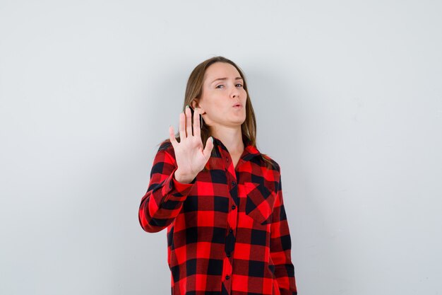 Jonge, mooie vrouw die een stopgebaar in een casual shirt toont en er zelfverzekerd uitziet. vooraanzicht.