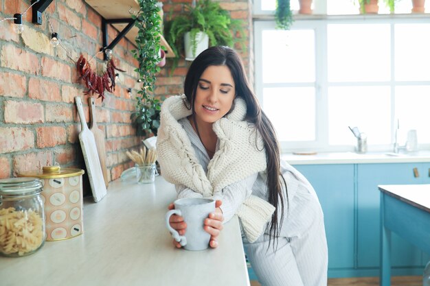 Jonge mooie vrouw die een warme drank in de keuken drinkt