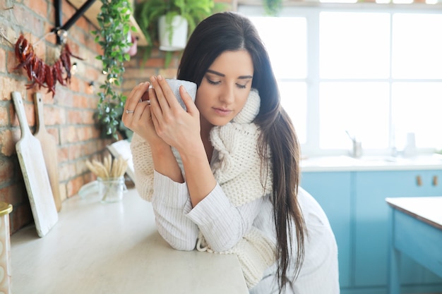 Jonge mooie vrouw die een warme drank in de keuken drinkt