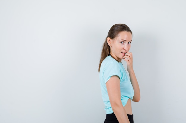 Jonge, mooie vrouw die haar nagels in een t-shirt bijt en er gestrest uitziet, vooraanzicht.