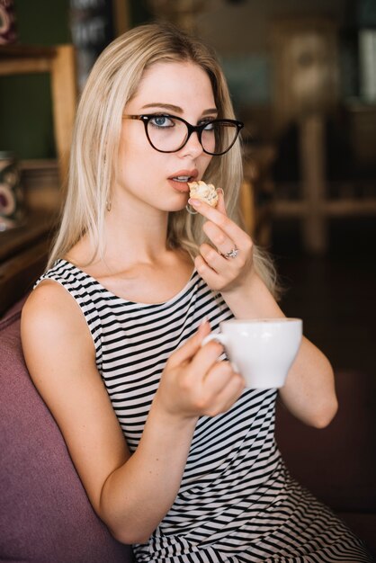 Jonge mooie vrouw die koekjes eet die koffiekop houden