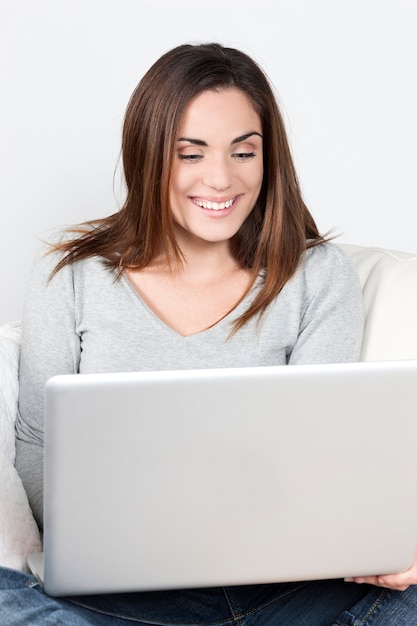 Jonge mooie vrouw die laptop op bank met behulp van