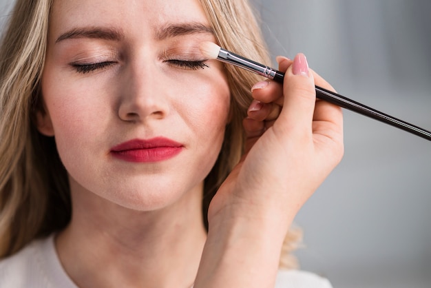 Jonge mooie vrouw die make-up toepast door borstel