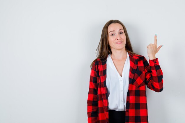 Jonge mooie vrouw die omhoog wijst in een casual outfit en er vrolijk uitziet. vooraanzicht.