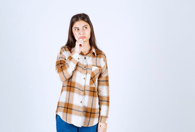 jonge mooie vrouw die over iets op witte muur denkt.