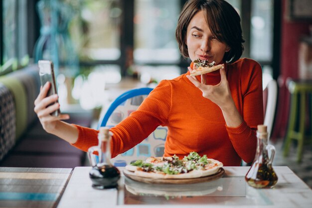 Jonge mooie vrouw die pizza eet bij pizzabar