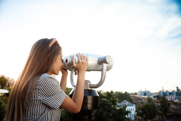 Jonge mooie vrouw die rond stad loopt, die door verrekijkers kijkt