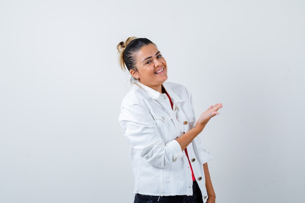 Jonge mooie vrouw die welkom gebaar in t-shirt, witte jas toont en er vrolijk uitziet. vooraanzicht.