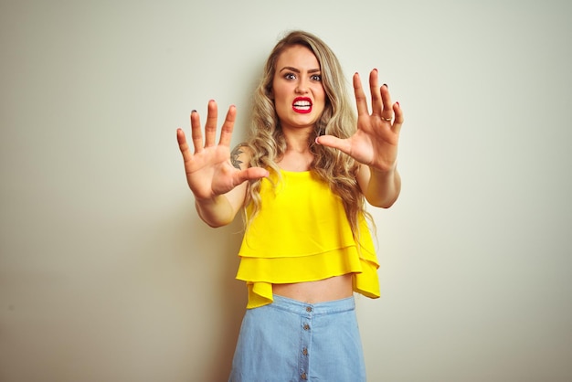 Jonge mooie vrouw, gekleed in een gele t-shirt die over een witte geïsoleerde achtergrond staat, bang en doodsbang van angstuitdrukking, stop gebaar met handen schreeuwend in shock Paniekconcept