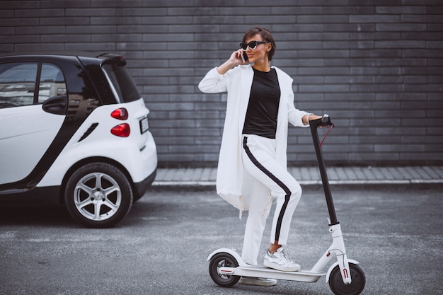 Jonge mooie vrouw gekleed in witte paardrijden scooter