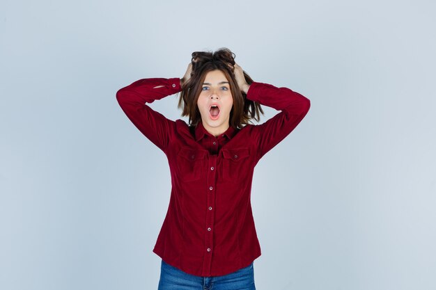 Jonge mooie vrouw hand in hand op het hoofd in shirt en ziet er bang uit.