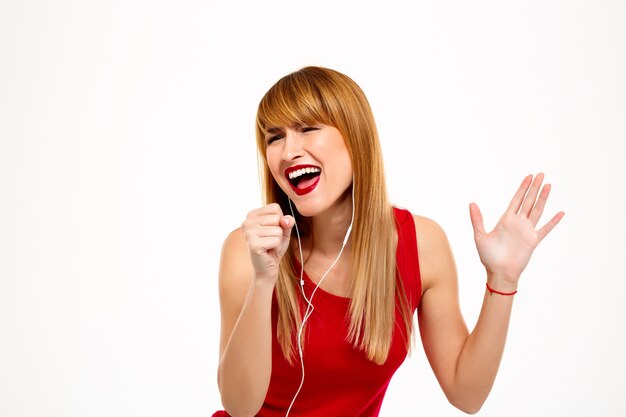 Jonge mooie vrouw het luisteren muziek in hoofdtelefoons over witte muur