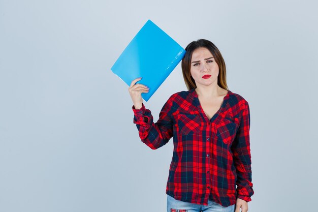 Jonge mooie vrouw houdt map in casual shirt en kijkt boos, vooraanzicht.