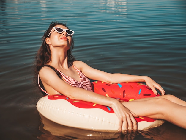 Jonge mooie vrouw in badkleding en zonnebril drijvend op de zee